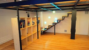 A room with a wooden floor, a staircase with a metal frame, and a bookshelf with books and a plant. - LOFT MADRID (Madrid)
