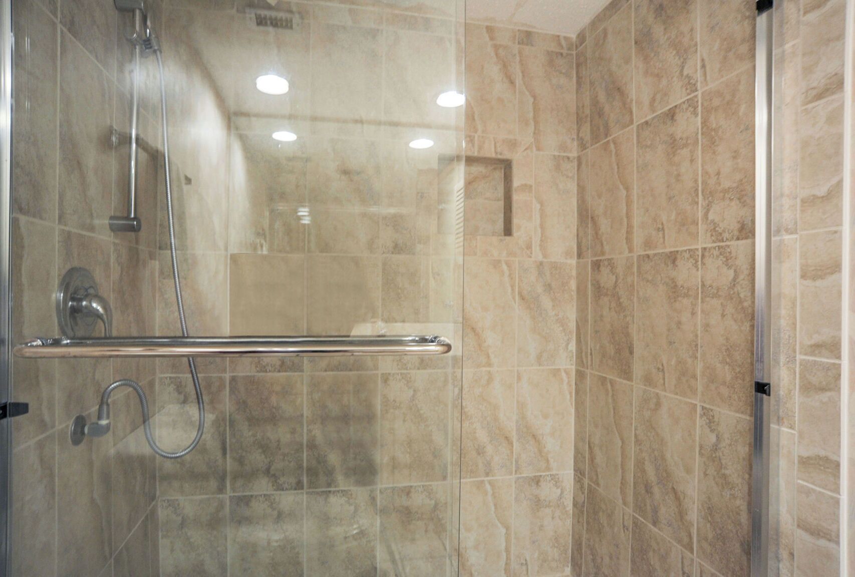 A modern shower with a glass door, a handrail, and a handheld showerhead.