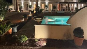 Un edificio grande y bien iluminado con piscina, palmeras y zonas de estar al aire libre.
