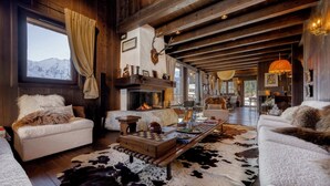L’intérieur chaleureux d’un chalet avec une cheminée, des meubles en bois et une vue sur les montagnes par la fenêtre.