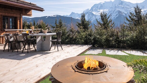 Une terrasse en bois avec un foyer, du mobilier d’extérieur et une vue sur des montagnes enneigées.