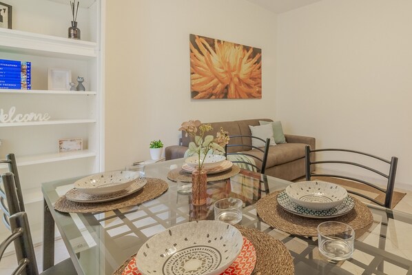 A dining table set with plates, bowls, and glasses, surrounded by chairs, with a sofa and a bookshelf in the background. - Le Foyer du Bizet in Lierna (Lierna)