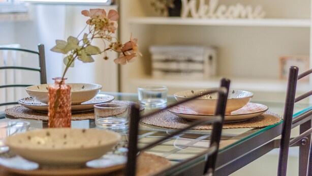 Een eettafel gedekt met borden, glazen en een vaas met bloemen.
