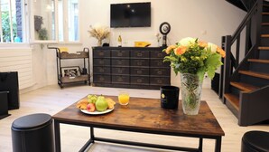Una cocina moderna con una mesa de madera, un florero de flores, un plato de fruta, un vaso de zumo de naranja y una taza negra.