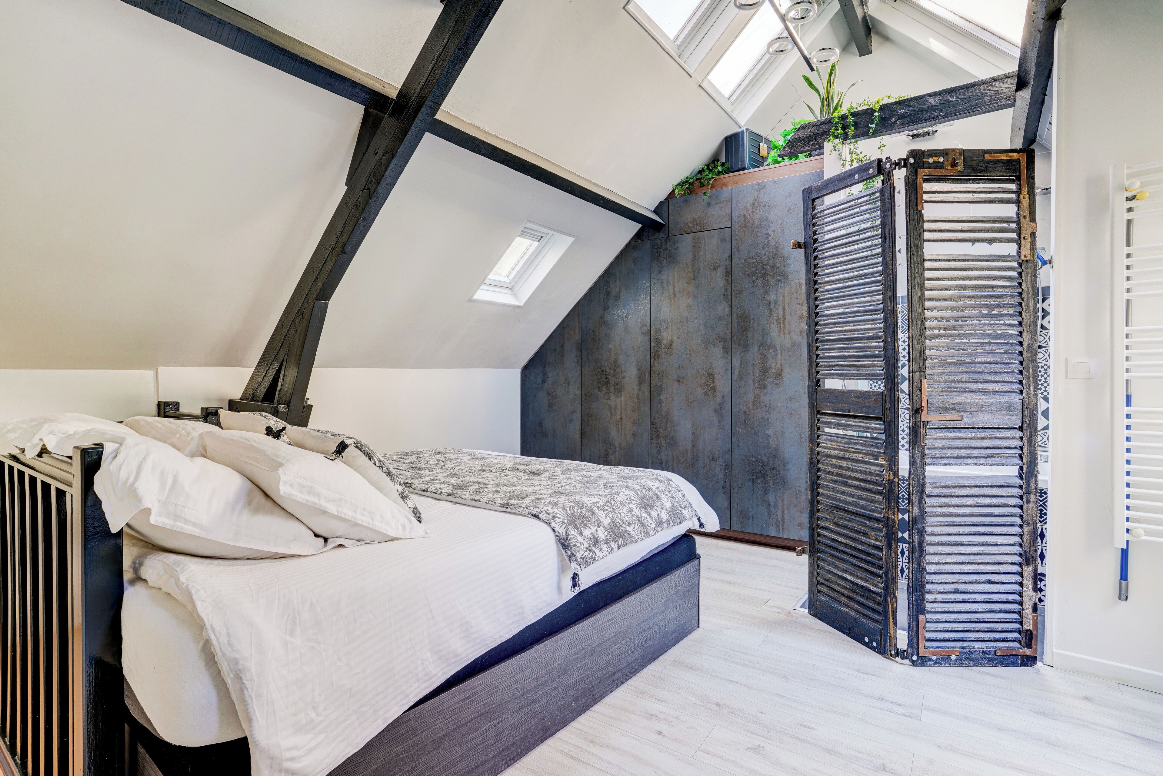 A bedroom with a sloped ceiling, a bed, a radiator, and a large window.