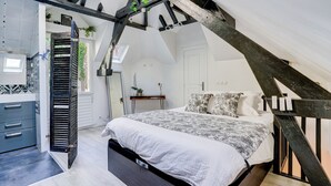 Un dormitorio con techo inclinado, una cama con ropa de cama estampada, un banco de madera y una mesita con una planta.