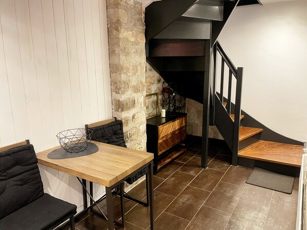 Un comedor con una mesa de madera y sillas acolchadas negras, una pared de piedra y una escalera con escalones de madera.