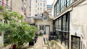 Un patio con un pequeño jardín, un espacio para sentarse y un edificio con amplias ventanas.