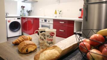 A kitchen with red cabinets, a washing machine, a coffee maker, and a fruit basket.