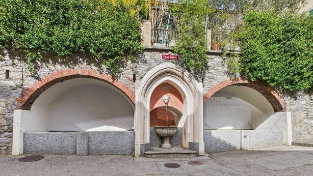 Une arche en pierre surmontée d’une fontaine centrale et d’une enseigne.