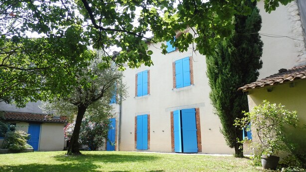 A building with multiple blue doors and windows, surrounded by greenery and a well-maintained lawn. - Le Numéro "4" - Charming house. (Labruguière)