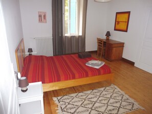A bedroom with a bed, a nightstand, a dresser, a window with curtains, a radiator, and a rug.
