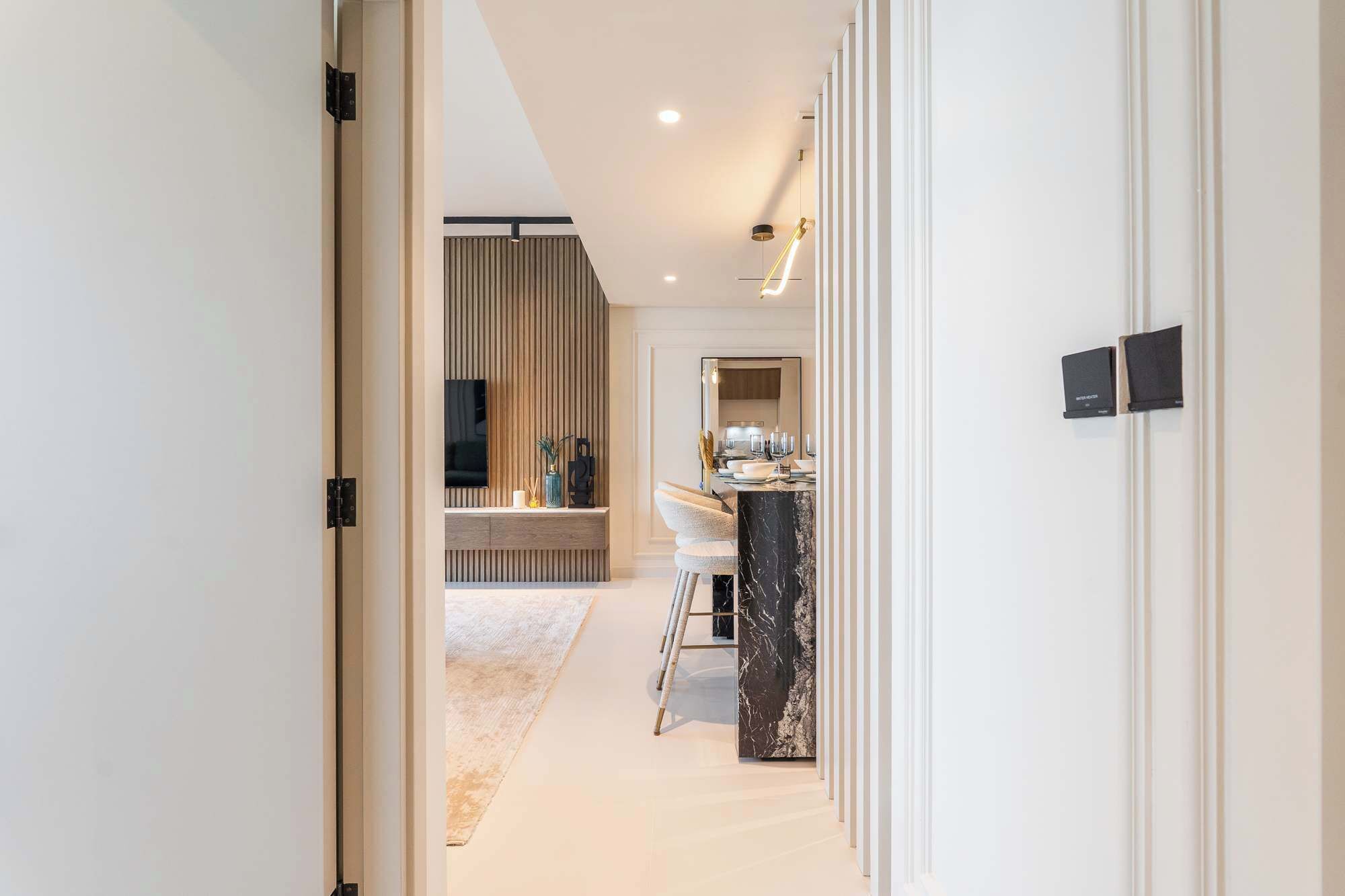 A modern hallway leading to a dining area with a marble table, a TV, and a wooden panel wall.
