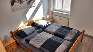 Una cama doble con estructura de madera, una mesita de noche con lámpara y un radiador.