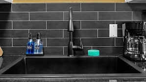 A kitchen with a black sink, two soap dispensers, a coffee maker, and a green sponge. - Joplin Avenue Junction: Two Bedroom Duplex (Tulsa)