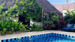A pool area with a tiled edge, surrounded by lush greenery and a thatched-roof structure. - Aurora Boutique Hotel (Jambiani)