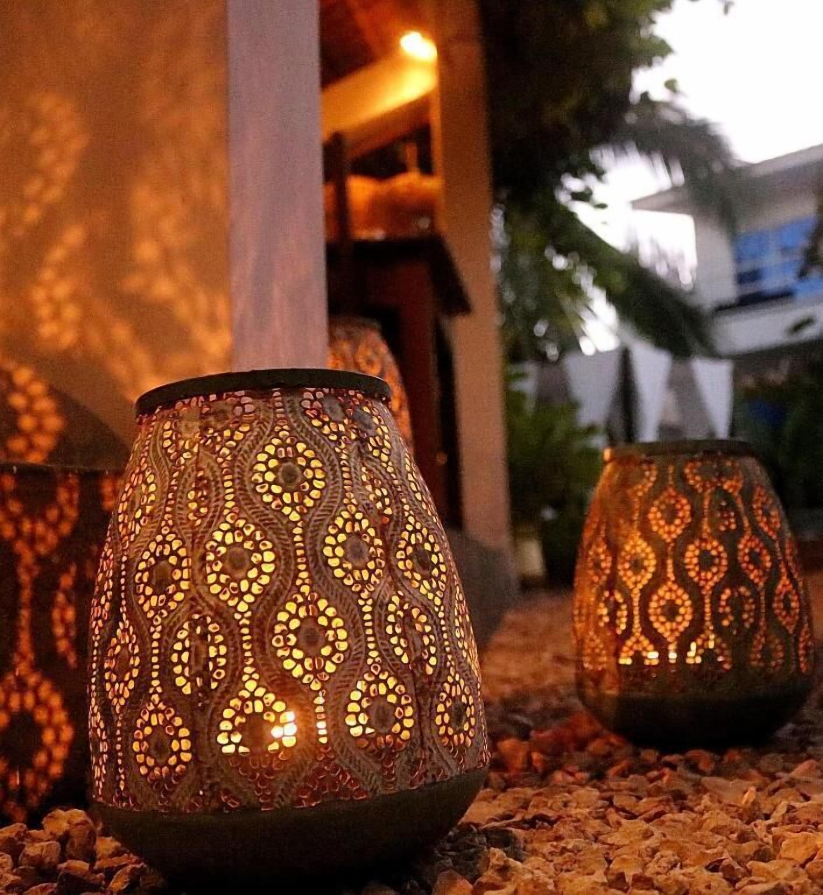A row of intricately designed lanterns with a patterned design, placed on a gravel surface outdoors.