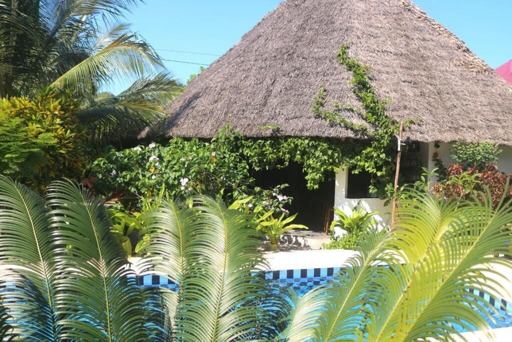 A thatched-roof structure surrounded by lush greenery and a swimming pool.