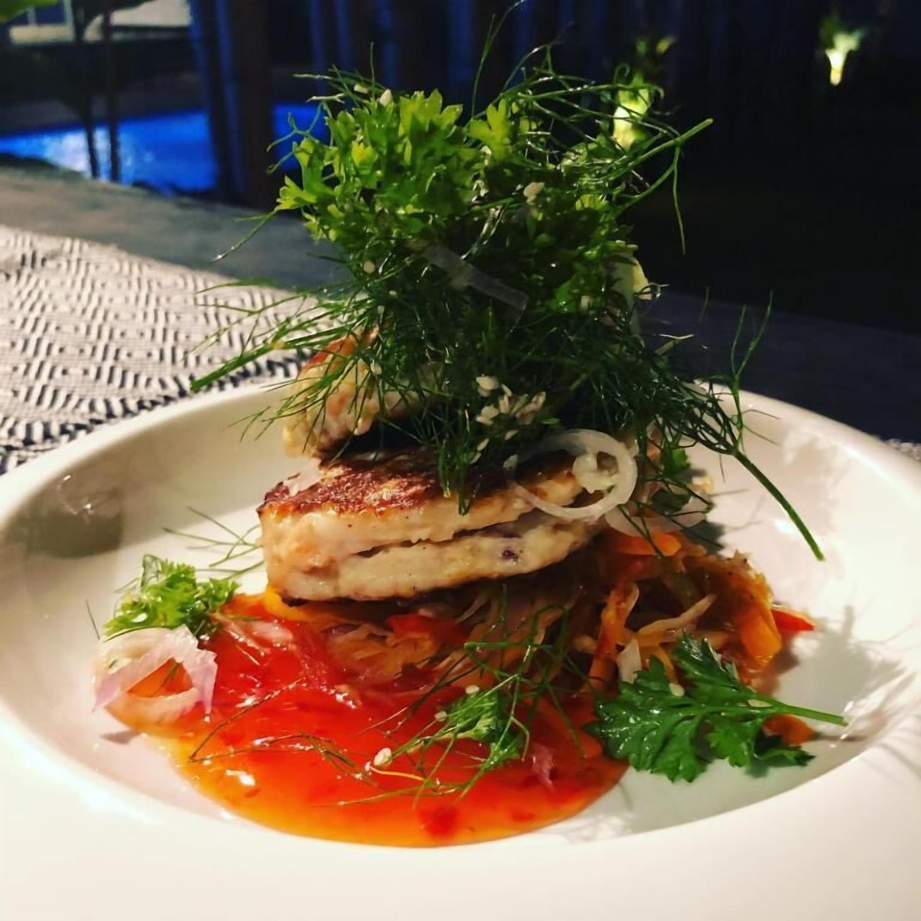 A plate of food with a garnish of green herbs and a red sauce.