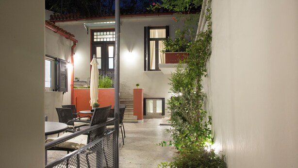 An outdoor patio area with tables and chairs, a small garden, and a staircase leading to an upper level. - Vol3 (Athens)