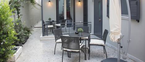 An outdoor patio with a round table and chairs, a small potted plant, and a white umbrella.