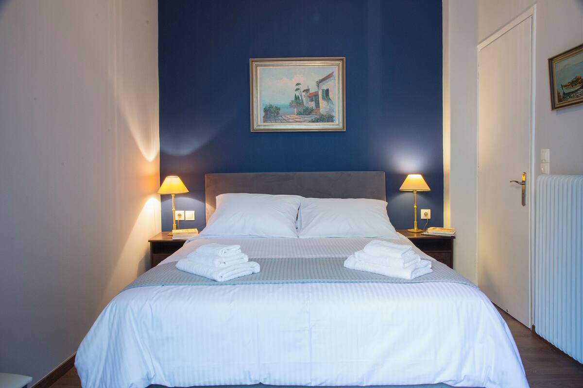 Ein ordentlich bezogenes Bett mit weißen Leinen, zwei Nachttischlampen und ein Bild an der Wand.