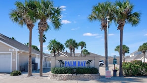Un quartier résidentiel avec une pancarte indiquant « PALM BAY VILLAGE », entouré de palmiers et de maisons.