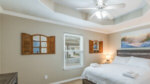 Une chambre à coucher avec un lit, un ventilateur de plafond, une fenêtre avec des stores et un tableau au mur.