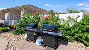 Un barbecue installé dans un jardin, avec une maison en arrière-plan.