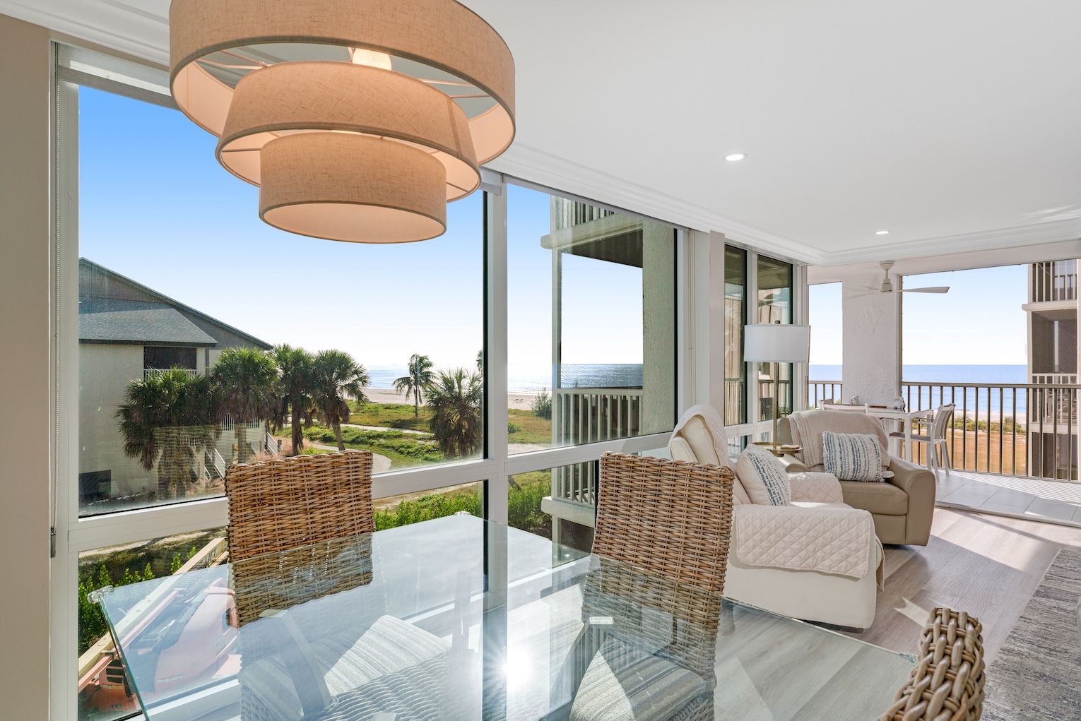 A spacious balcony with a glass table, wicker chairs, and a sofa overlooking a beach.