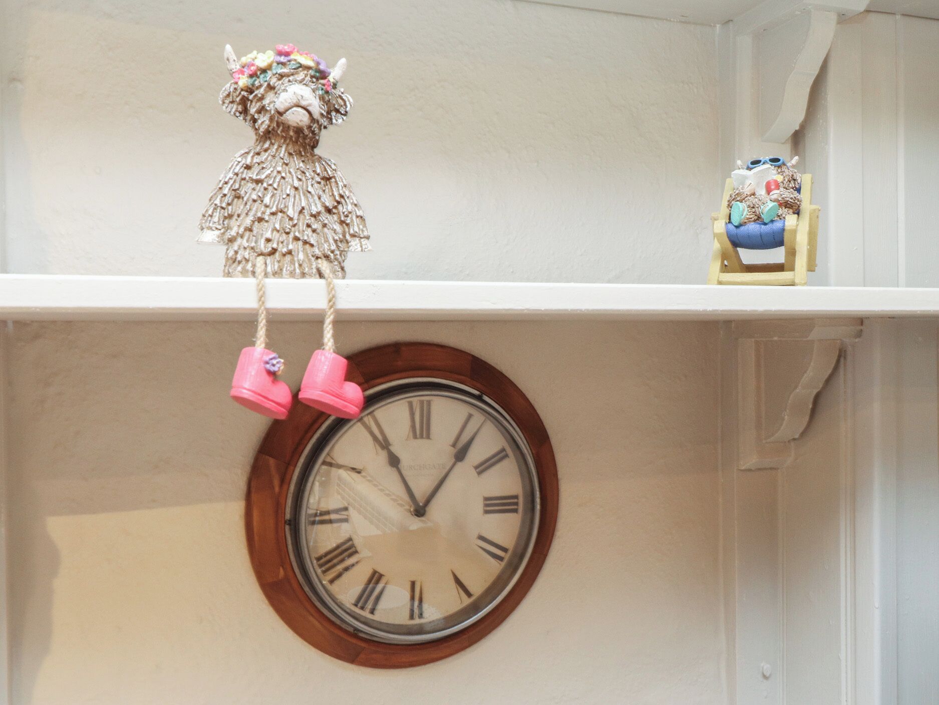 A wall clock with Roman numerals and a decorative hanging ornament above it.