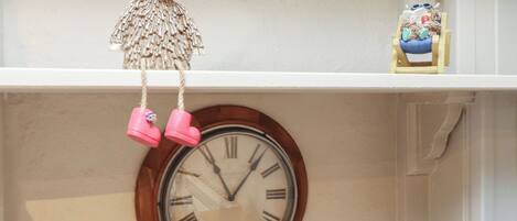 A wall clock with Roman numerals and a decorative hanging ornament above it.