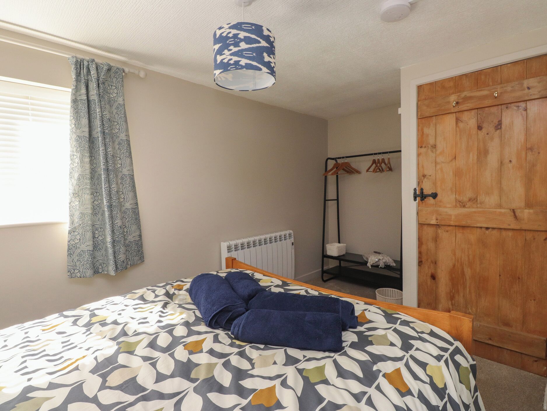 A bedroom with a bed, a radiator, a wooden wardrobe, and a hanging clothes rack.