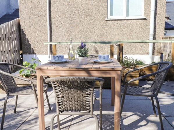 An outdoor seating area with a wooden table and wicker chairs, a bottle of wine, and a bowl on the table. - Hafod (Pwllheli)