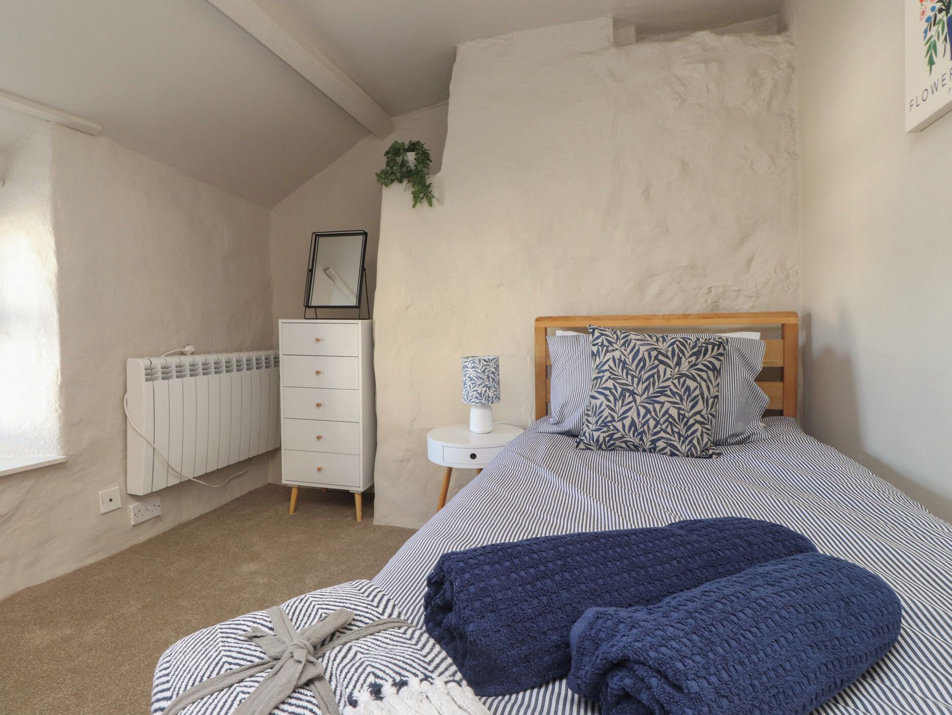 A bedroom with a bed, a dresser, a radiator, and a small bedside table with a lamp.