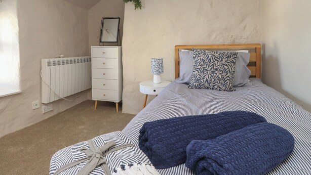 A bedroom with a bed, a dresser, a radiator, and a small bedside table with a lamp. - Hafod (Pwllheli)
