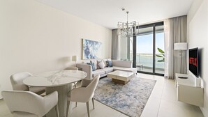 Un salon moderne comprenant un coin repas, un ensemble de canapés, un téléviseur à écran plat et une grande fenêtre donnant sur la mer.