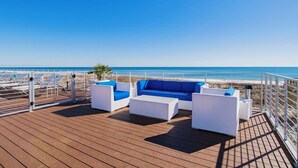 A deck with white wicker furniture and a view of the beach.