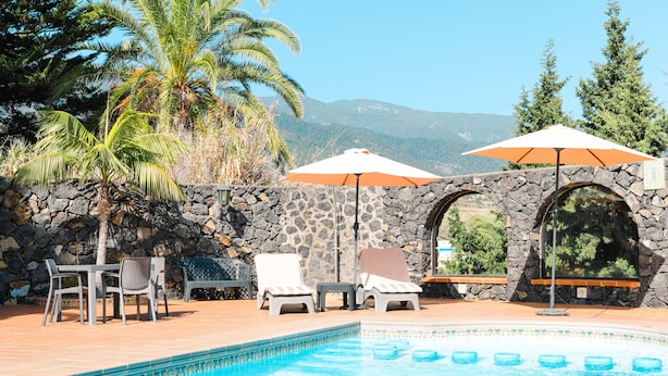 Un área de piscina con sillas de descanso, sombrillas y un muro de piedra.