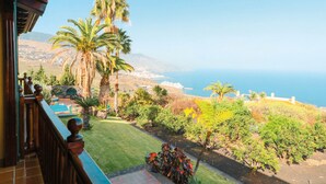 Un balcón con vista al océano y un jardín ajardinado con palmeras y arbustos.