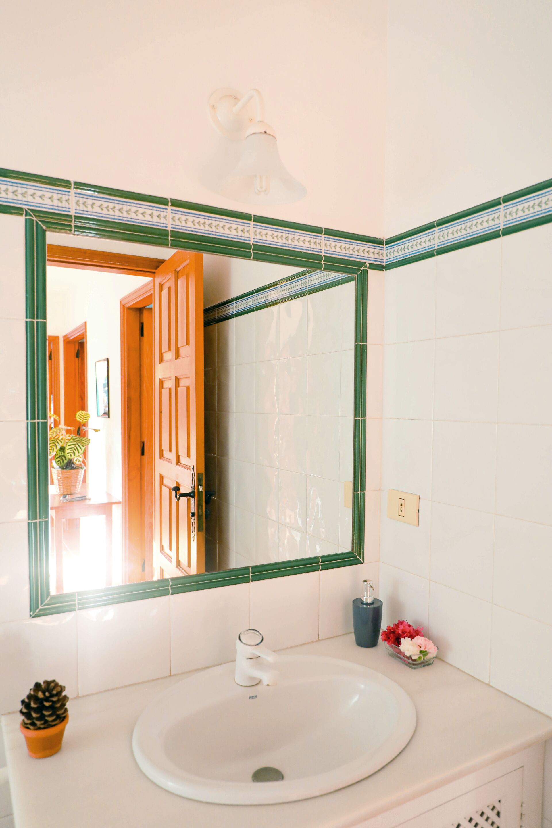 A bathroom with a white sink, a mirror with a green frame, and a potted plant.