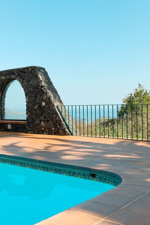 A stone archway leading to a pool area with a clear view of the sea.