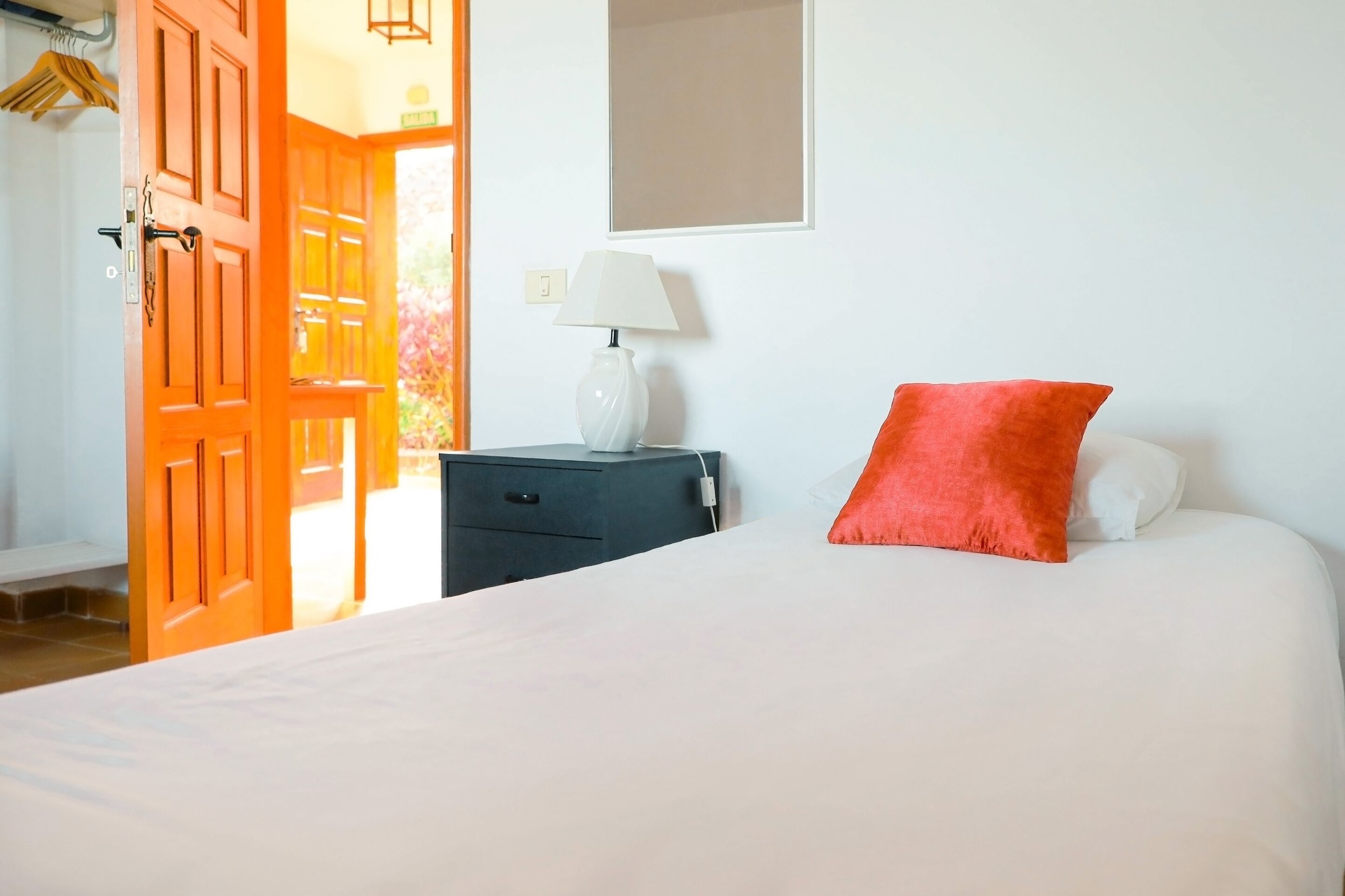 A bedroom with a bed, a nightstand, a lamp, and an open door leading to another room.