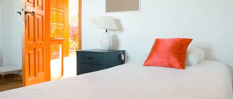 A bedroom with a bed, a nightstand, a lamp, and an open door leading to another room.