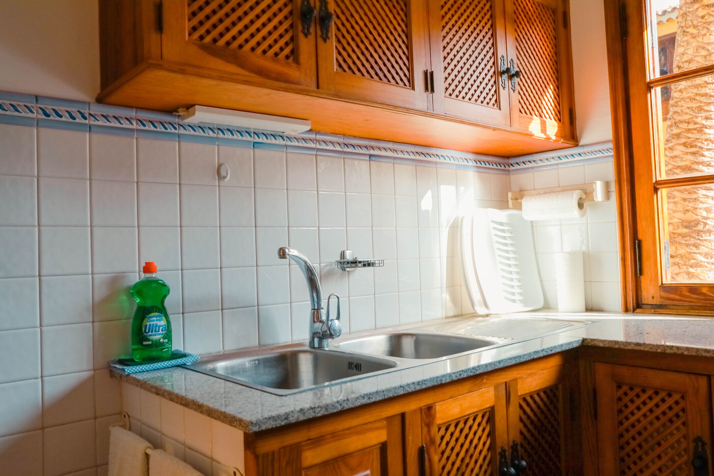 A kitchen with wooden cabinets, a stainless steel sink, and a tiled backsplash.