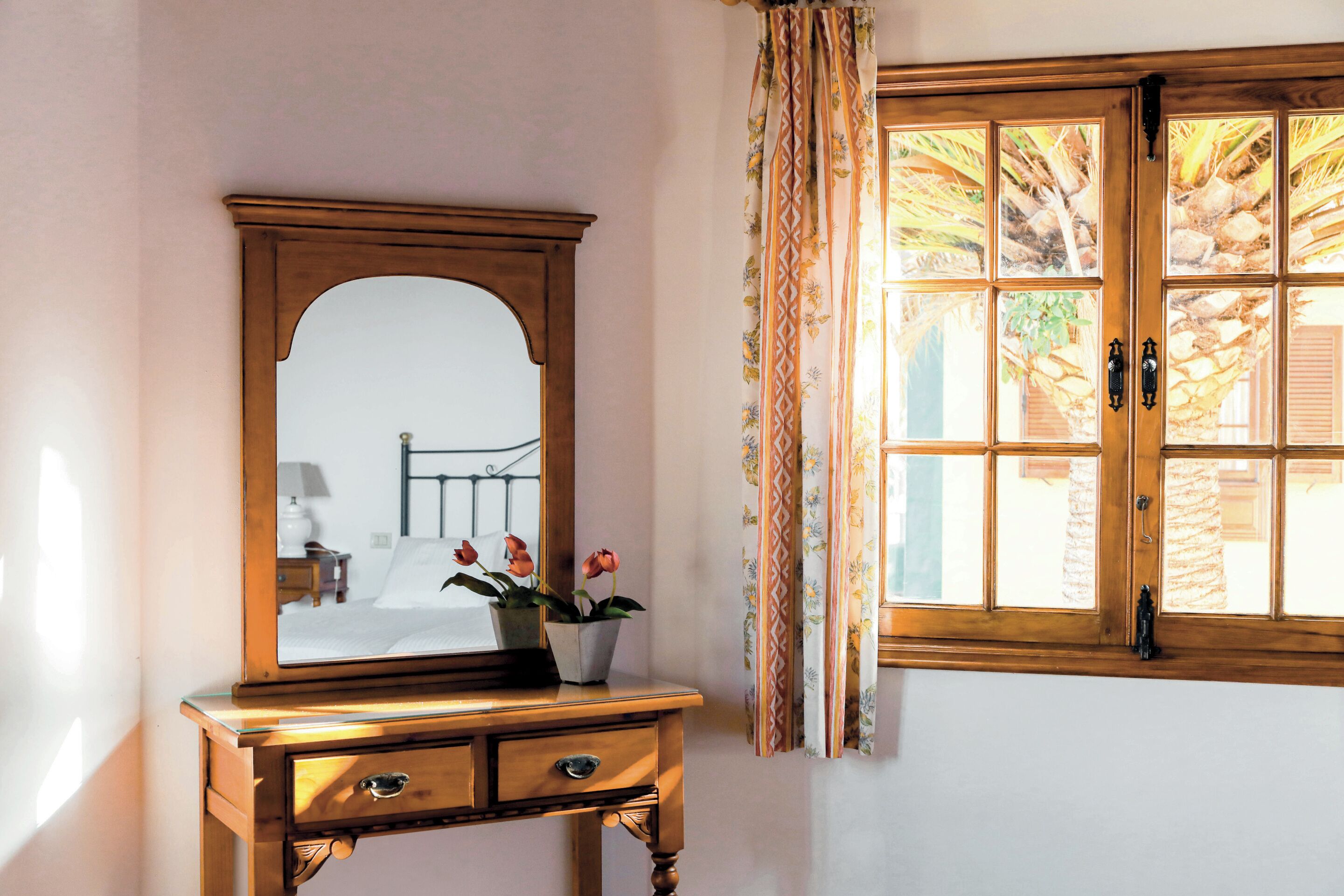 Una mesita de noche de madera con un espejo, una pequeña planta en maceta y una ventana con cortinas.