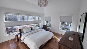 A bedroom with a large bed, a wooden dresser, a chair, and a large window with blinds. - New construction, 4-bedroom house with, fitness room in lovely Bridgehampton (Bridgehampton)