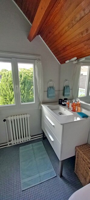 A bathroom with a white sink, two towel rings, a radiator, a window with curtains, and a view of greenery outside. - A peaceful getaway between Paris and Disneyland—2 comfortable rooms with a garden (Chennevières-sur-Marne)