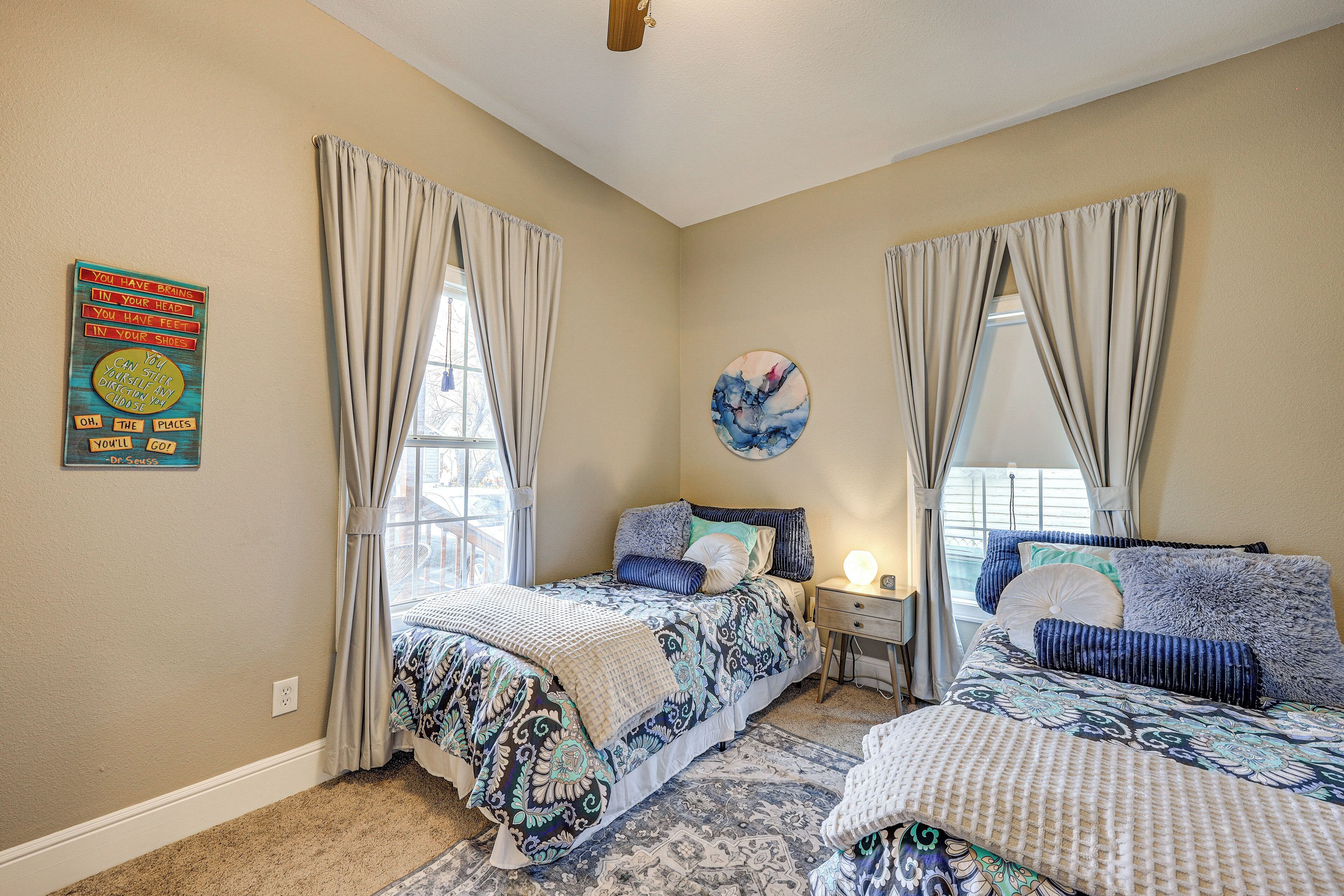 A bedroom with two beds, beige walls, and a large window with curtains.