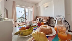 Un coin repas avec une table mise pour le petit-déjeuner, comprenant des fruits, un beignet et un verre de jus d’orange.